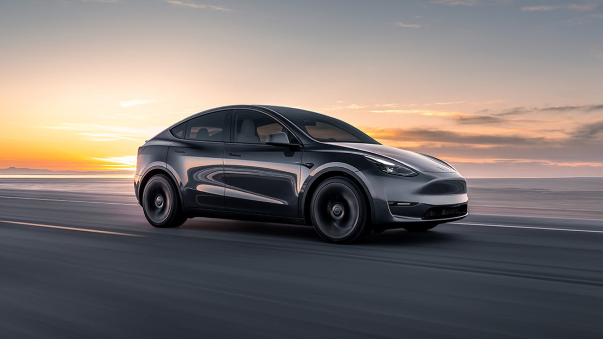 Gray Tesla Model Y driving beside the water at sunset in an official Tesla image